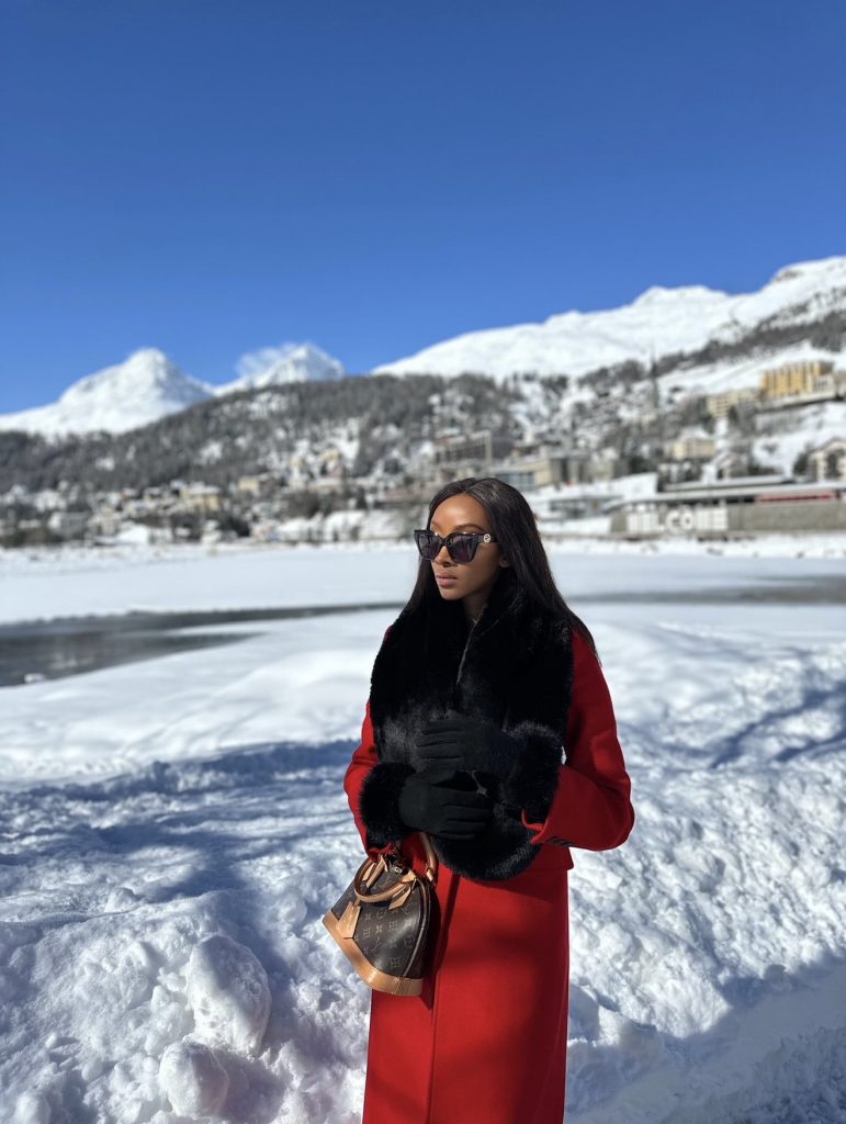 Solo female traveler standing in the snow in St Moritz in winter, with mountains and blue sky in the background.