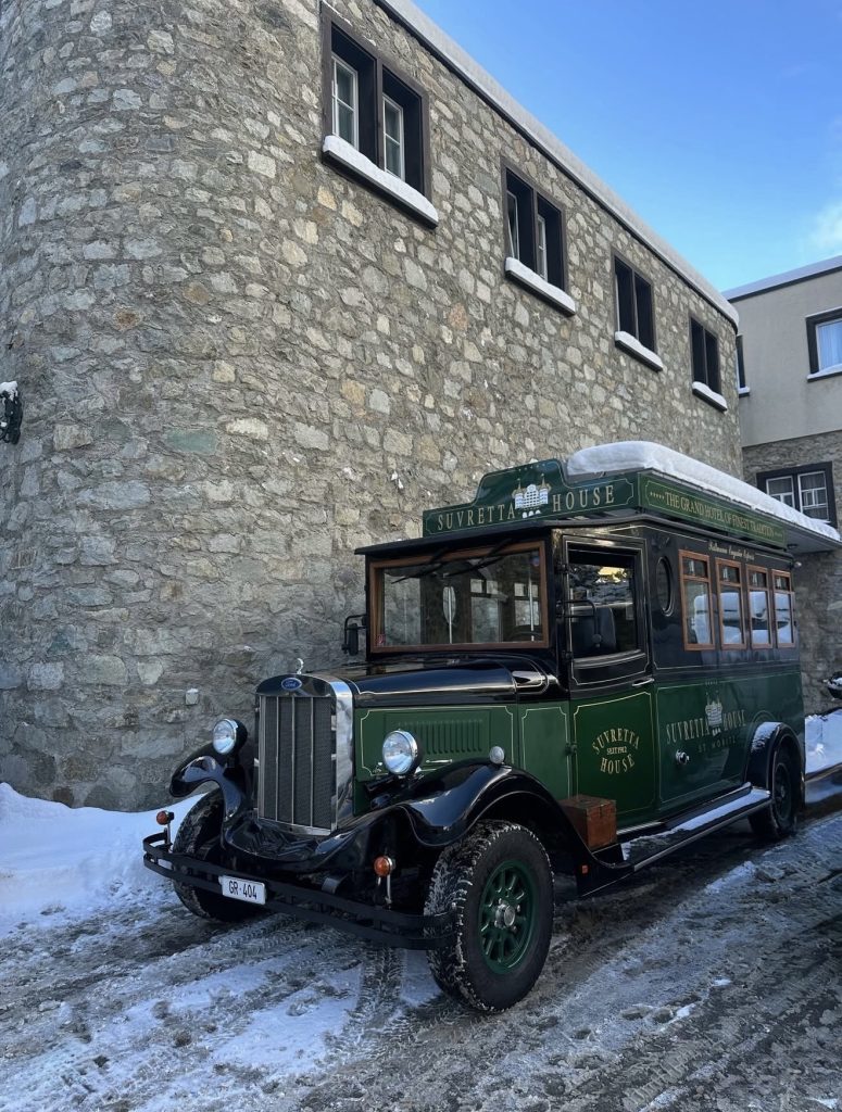 Vintage Suvretta House hotel shuttle bus parked outside the stone building in St Moritz during winter.