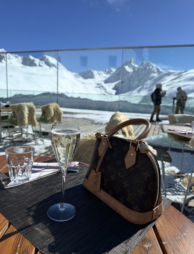 Glass of champagne on an outdoor mountain terrace in St Moritz in winter, with snowy alpine views in the background.