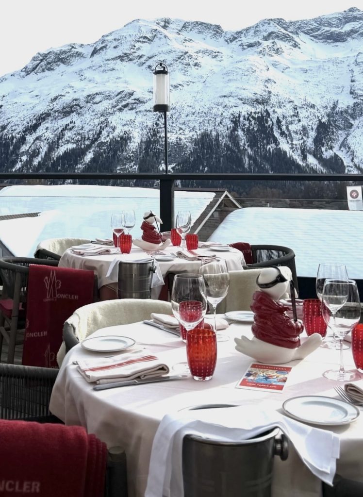 Outdoor restaurant terrace in St Moritz in winter, with set dining tables and snowy mountain views in the background